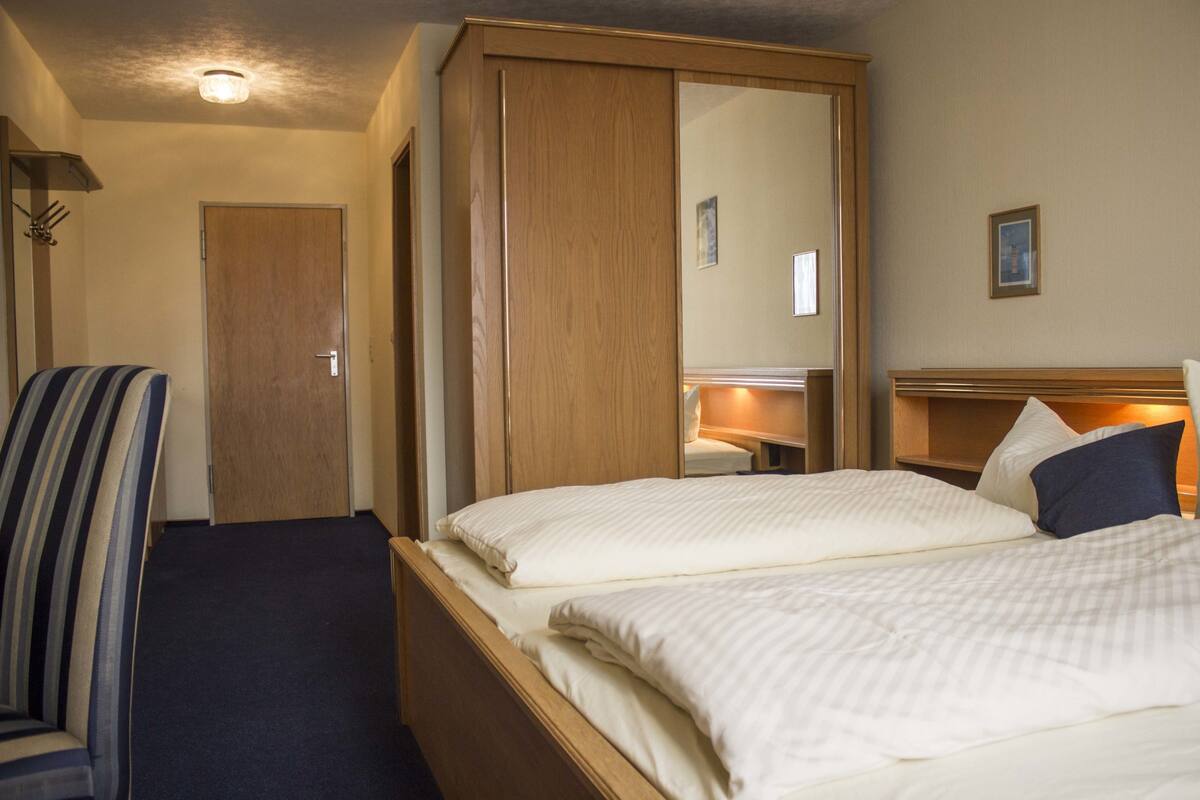 A hotel room with a bed, a chair, a wardrobe, and a mirror.