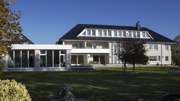 A two-story building with a large balcony, a covered patio, and a well-maintained lawn. - Hotel Am Friesenstrand (Butjadingen)