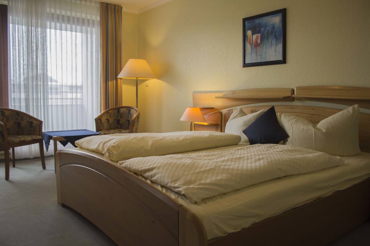 A hotel room with a double bed, a desk, a chair, and a lamp.