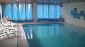 An indoor swimming pool with clear blue water, white lounge chairs, and a tiled floor. - Hotel Am Friesenstrand (Butjadingen)