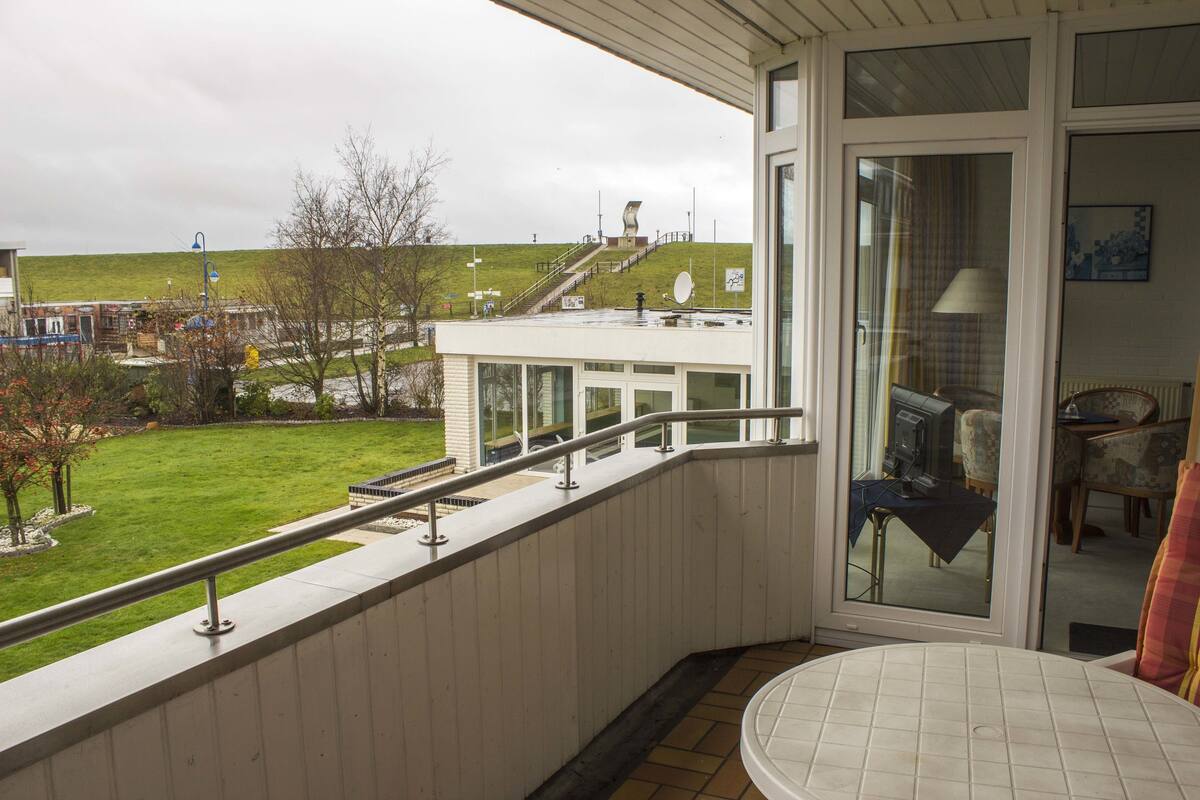 A balcony with a view of a grassy hill and a building in the distance.