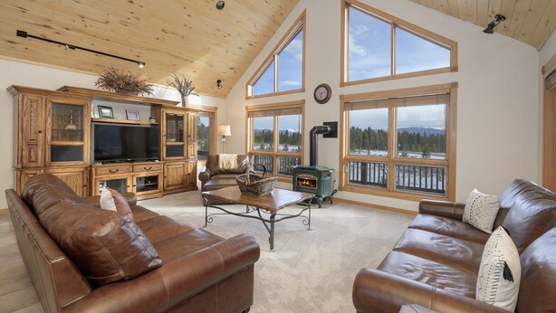 A spacious living room with leather sofas, a wooden entertainment unit, and large windows offering a view of a snowy landscape.