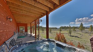 A hot tub under a wooden pergola with a view of a grassy field and trees.