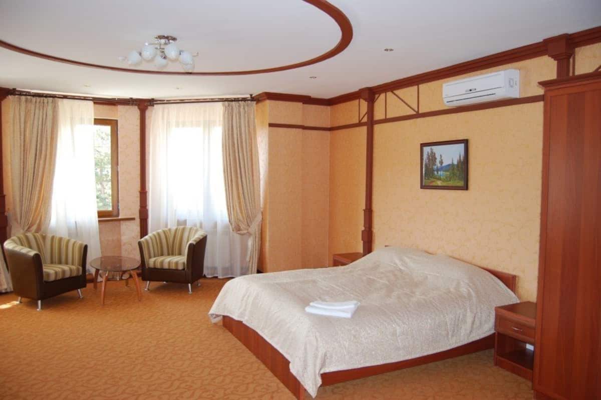 A hotel room with a large bed, two armchairs, a small table, and a window with curtains.
