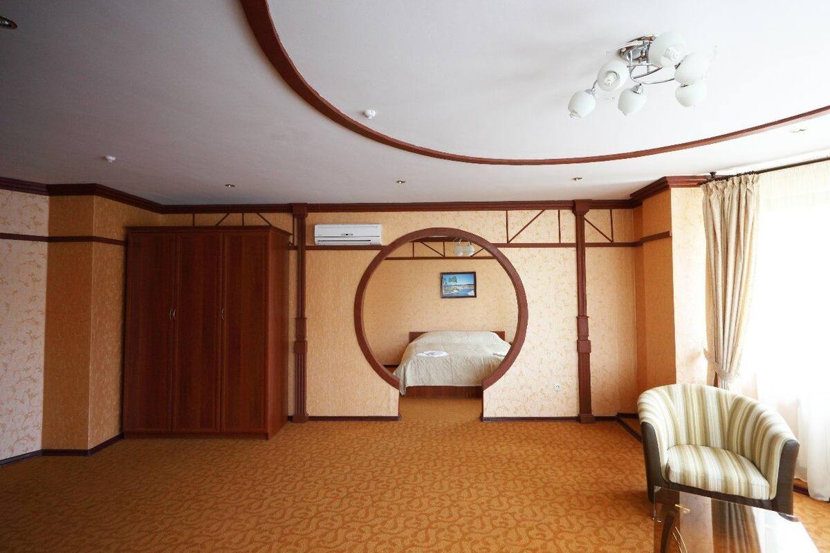 A hotel room with a bed, a wooden wardrobe, a circular archway, a chair, and a ceiling light fixture.