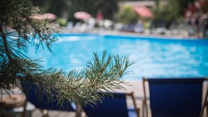 Piscina com espreguiçadeiras e guarda-sóis ao fundo.