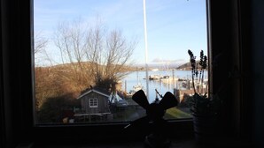 A view from a window overlooking a body of water with boats, a dock, and a small house in the background. - Brännö Varv Bed & Breakfast (Branno)
