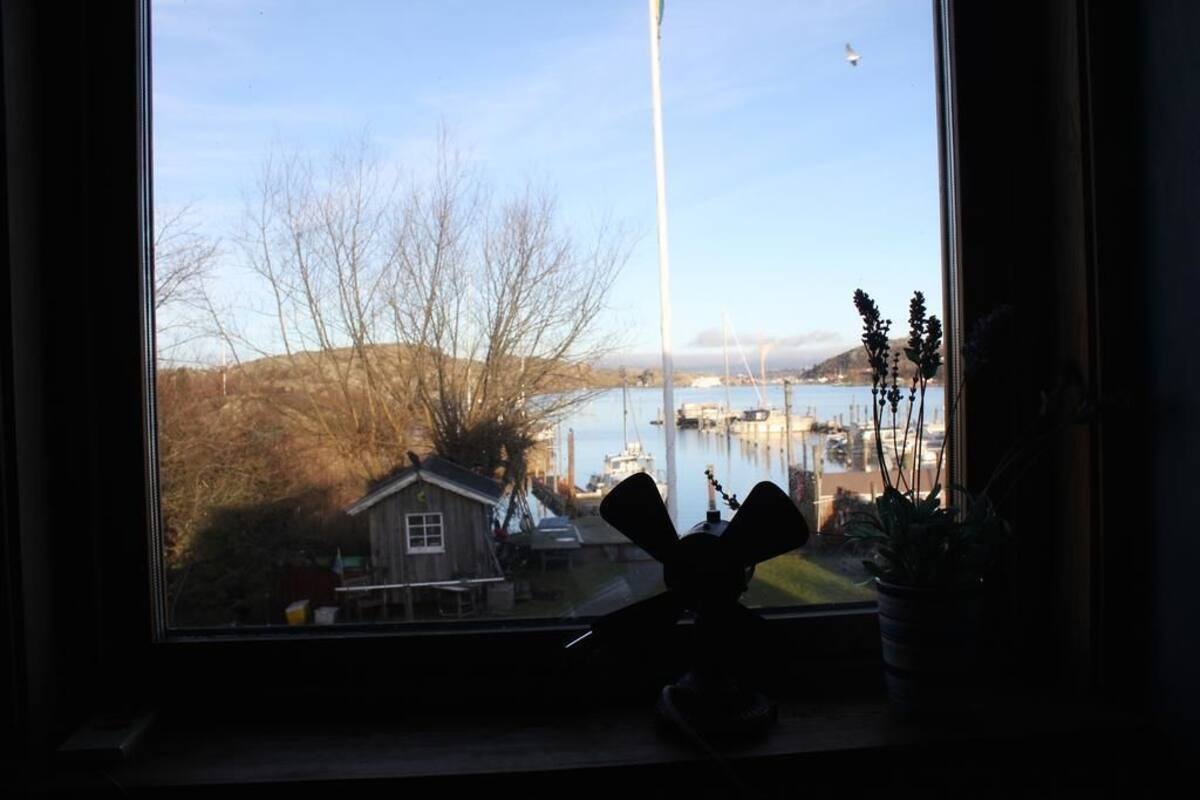 A view from a window overlooking a body of water with boats, a dock, and a small house in the background.
