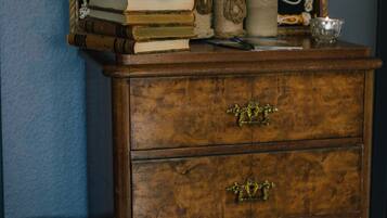 A wooden chest of drawers with brass handles, a blue vase, and a framed crochet pattern on the wall behind it.