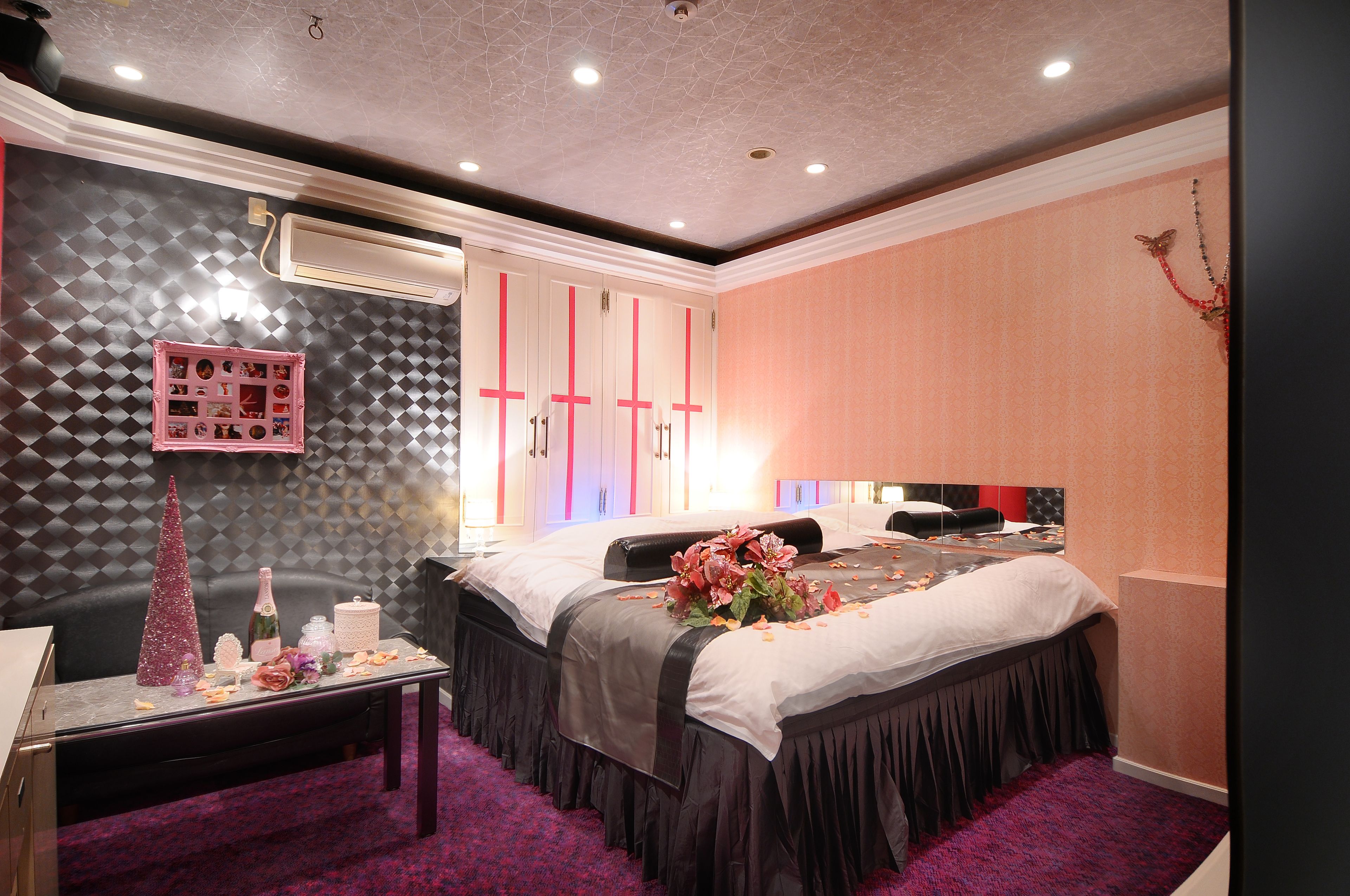 Quarto de hotel com cama, penteadeira, espelho e cômoda com armário rosa.