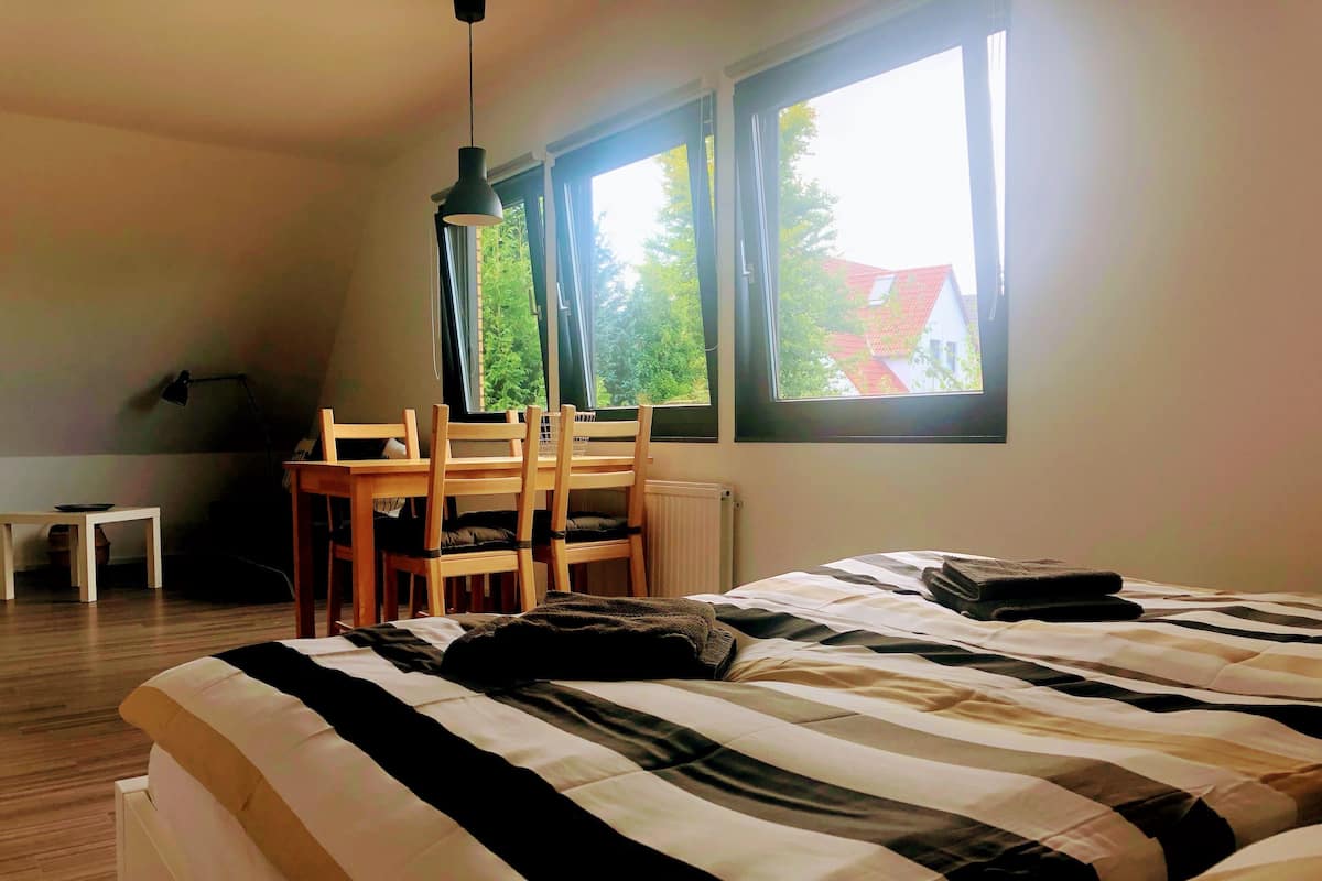 A bedroom with a large bed, a wooden desk, and two windows.
