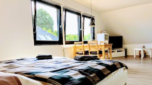 A bedroom with a bed, a desk, a chair, a TV, and large windows. - Appartements Summer Break (Scharbeutz)