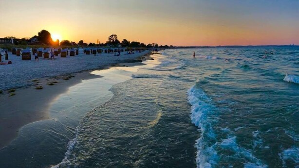 A beach with a row of beach huts and a sunset in the background. - Appartements Summer Break (Scharbeutz)