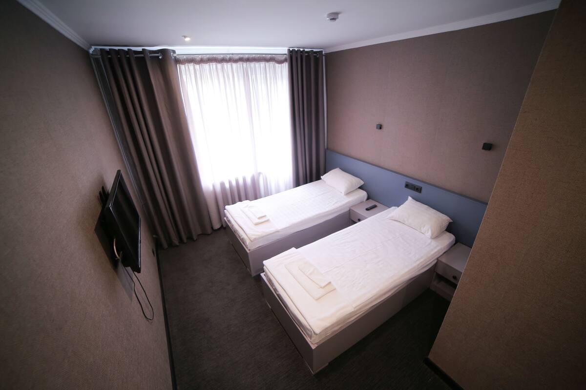 A hotel room with two single beds, a TV, and a window with curtains.