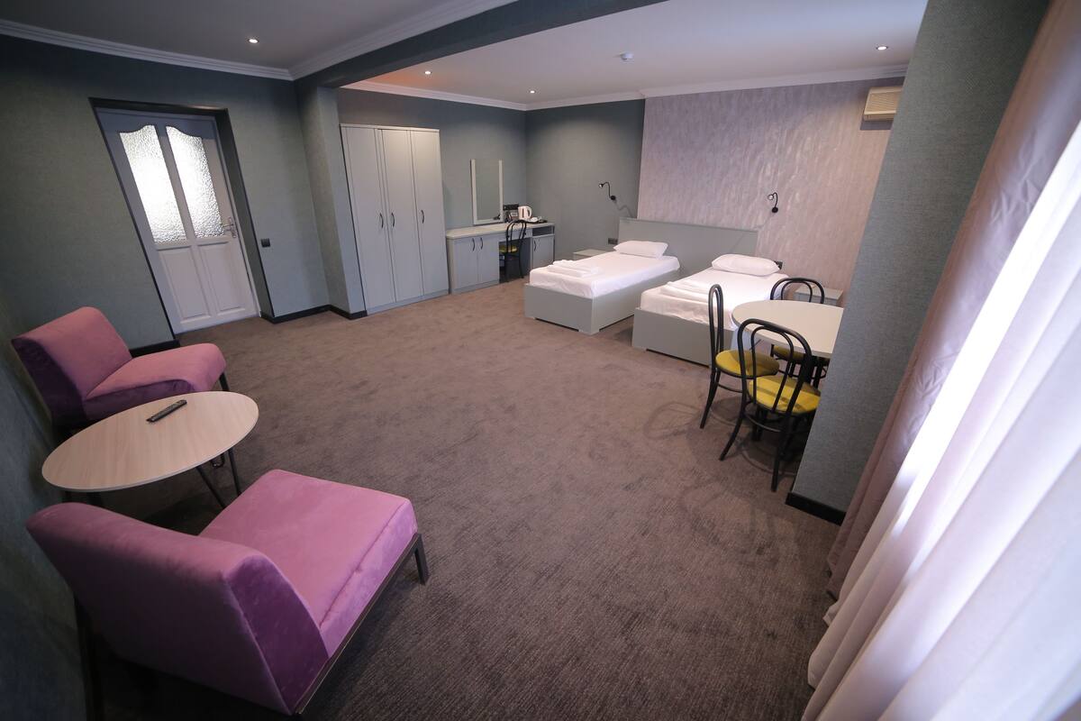 A modern hotel room with a sofa, a small table, a bed, a desk, and a wardrobe.