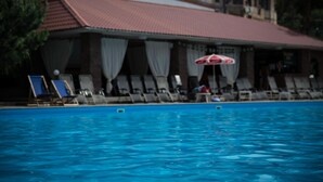 Una piscina con sillas de descanso y sombrillas, un edificio con techo rojo y un letrero.