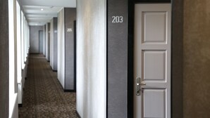 Un pasillo de hotel con piso alfombrado, varias puertas numeradas y un diseño moderno.