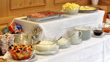Uma mesa de buffet com diversos alimentos, incluindo salada de frutas, iogurte e uma travessa de carnes.
