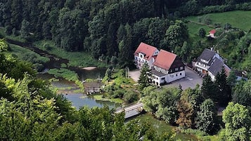 Una casa di campagna con tetto rosso immersa nel verde e bagnata da un fiume.