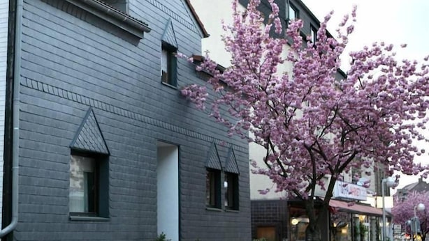 Un edificio con facciata grigia e un albero con fiori rosa in primo piano.