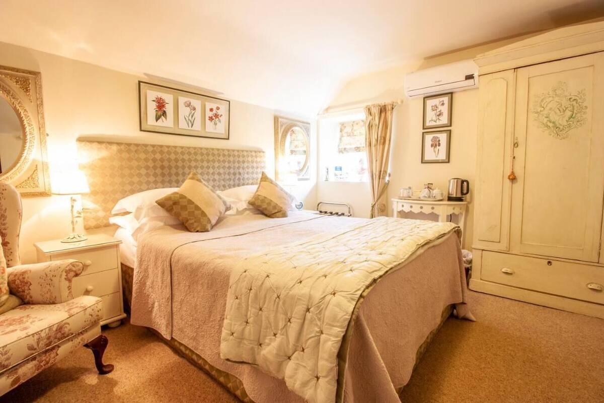 A bedroom with a large bed, a nightstand, a chair, a wardrobe, and a mirror.