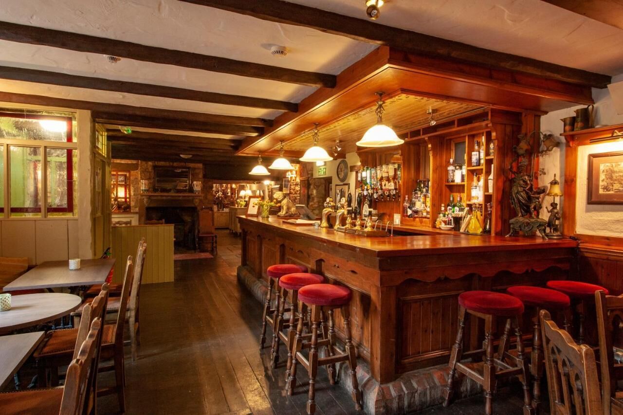 Eine Bar mit Holzbalken, einer Theke mit Hockern und Regalen voller Flaschen.