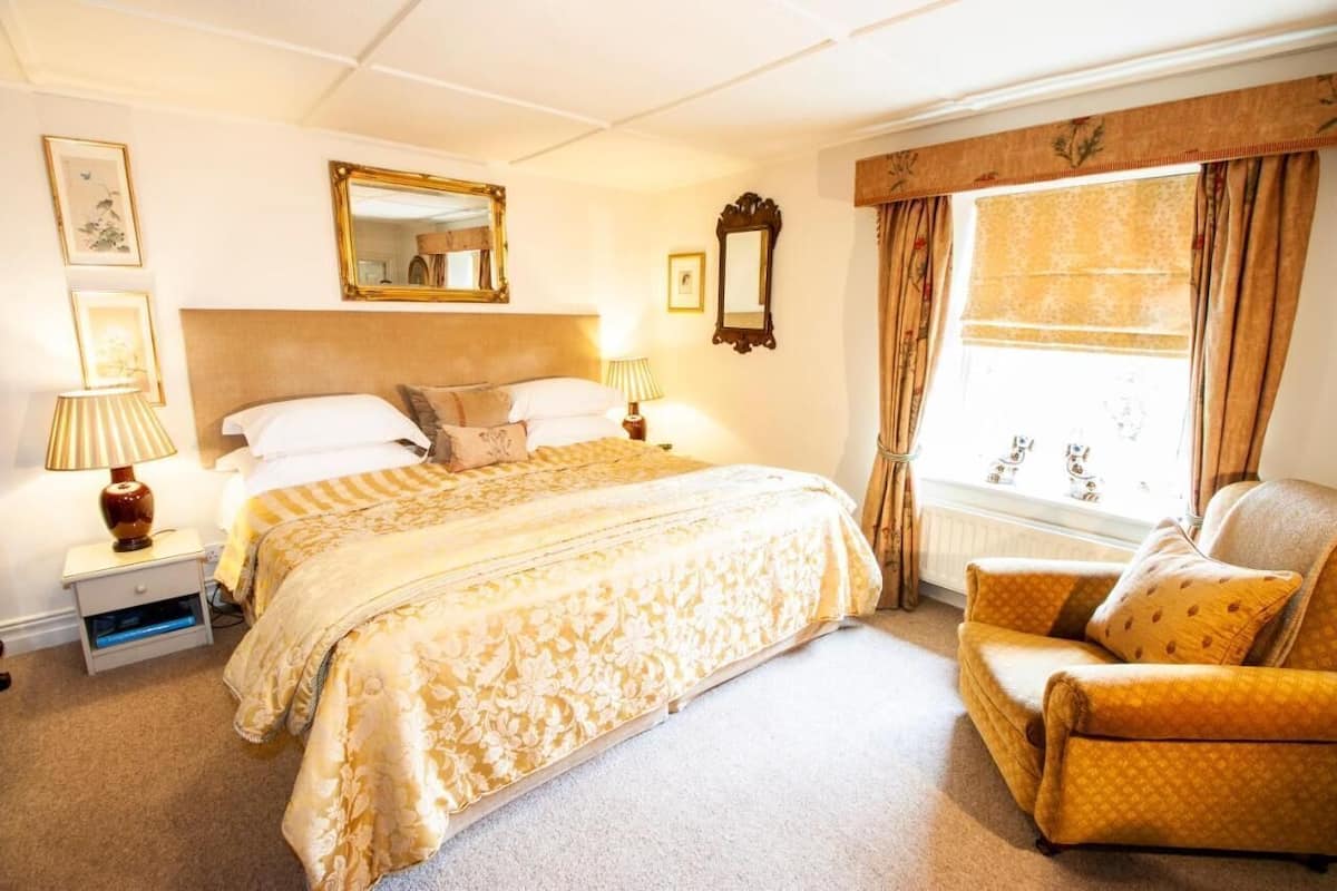 A hotel room with a large bed, a chair, a window with curtains, and a mirror on the wall.