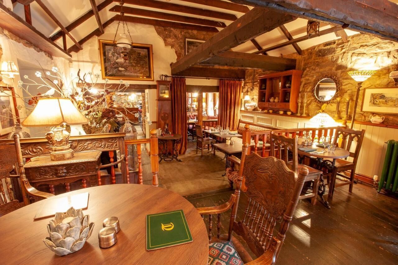 A rustic dining area with wooden furniture, a chandelier, and a stone wall.