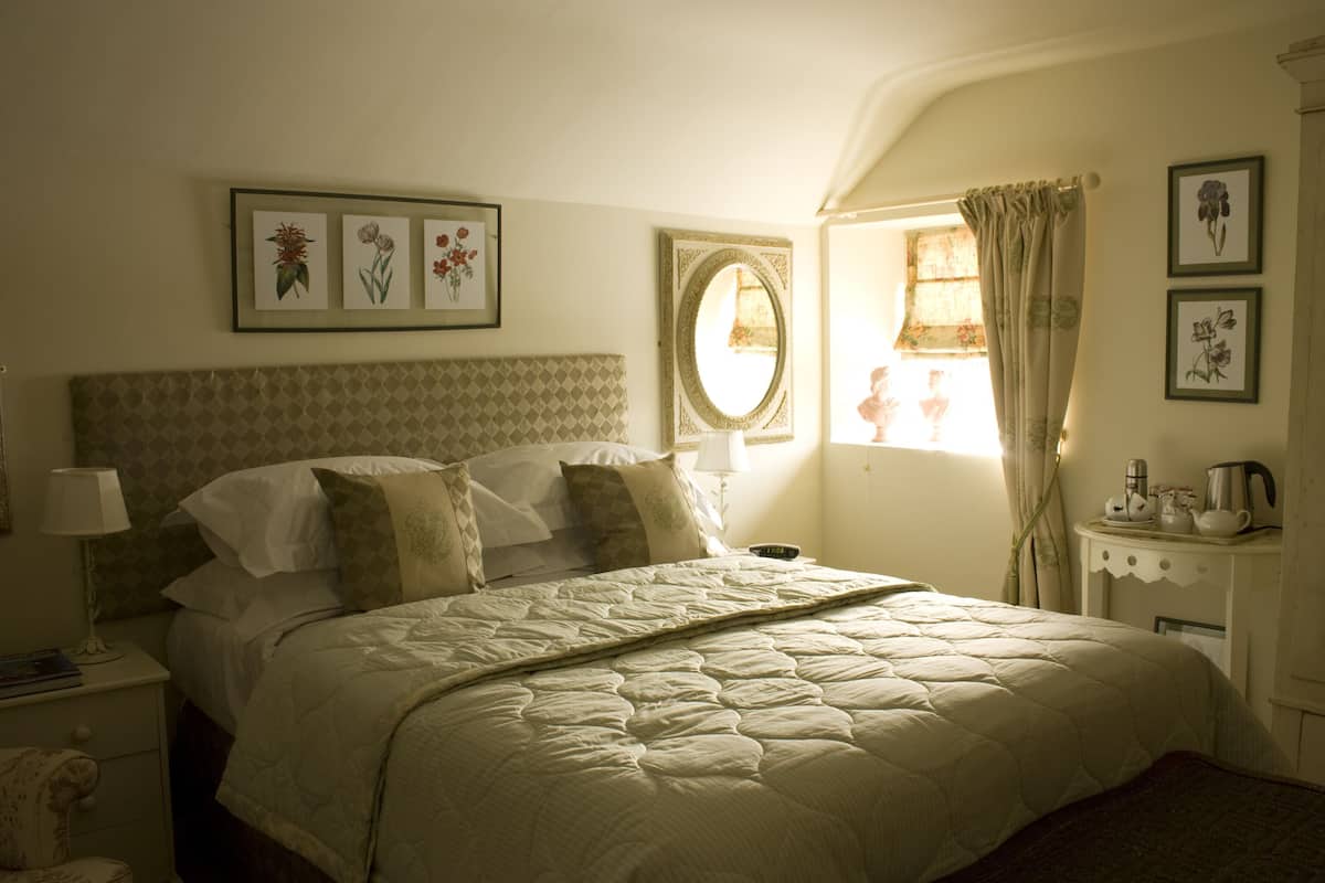 A bedroom with a large bed, a nightstand with a lamp, a dresser, and framed floral artwork on the wall.