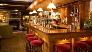 Eine Bar mit hölzernen Barhocker, einem Kamin und einer Auswahl an Flaschen und Gläsern auf Regalen.