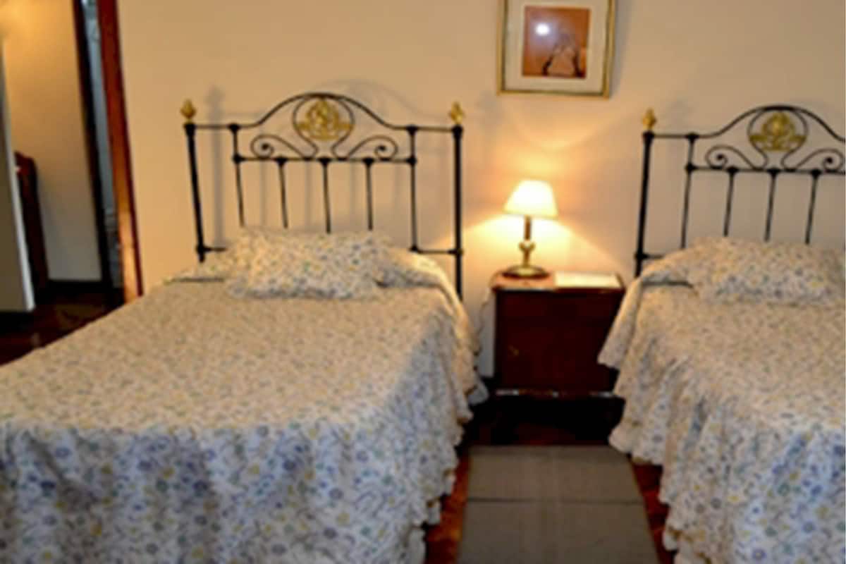 A room with two beds, each with a metal headboard and a bedside table with a lamp.