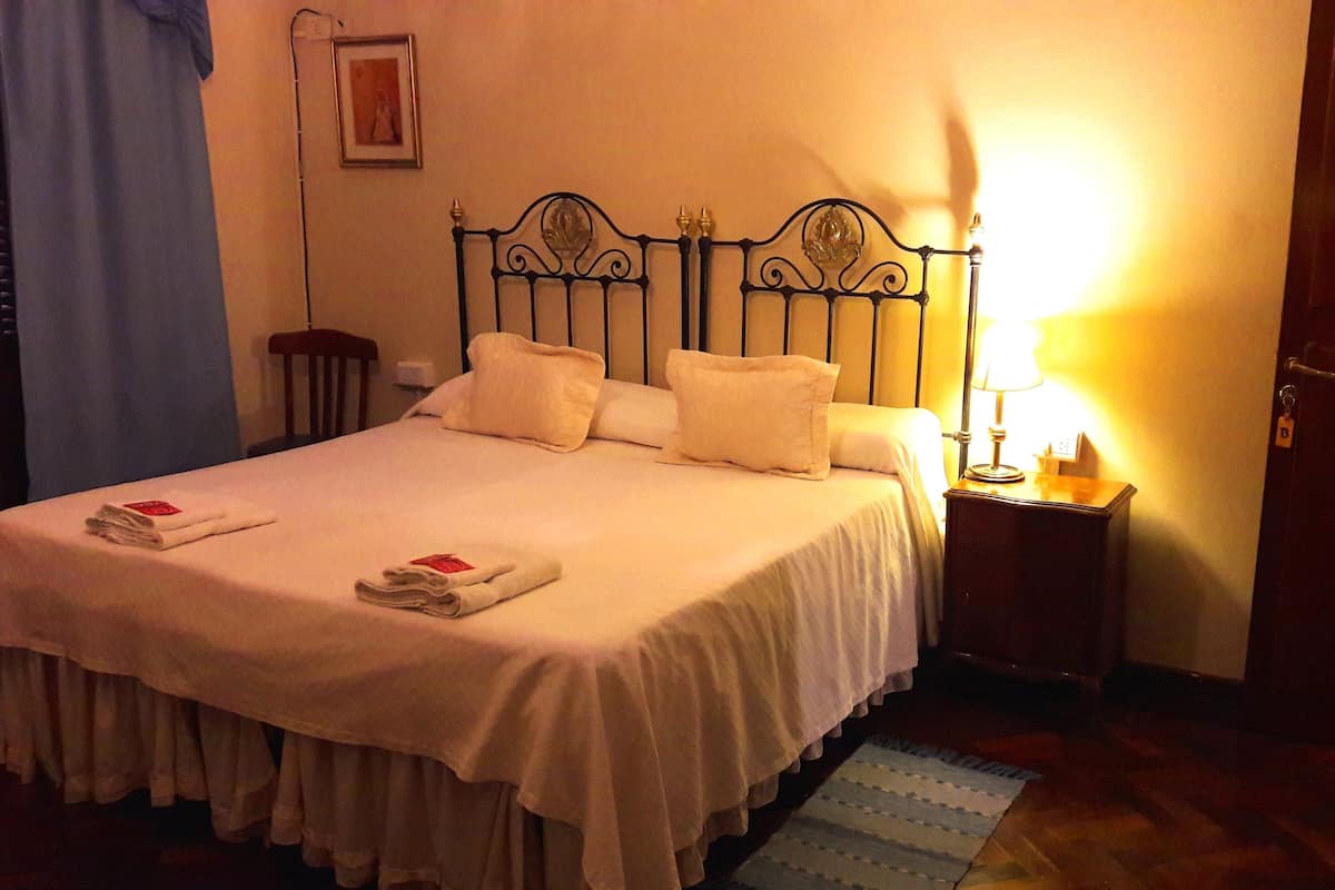 A neatly made bed with white linens and pillows, a bedside table with a lamp, and a framed picture on the wall.