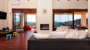 A spacious living area with a sofa, colorful stools, a flat-screen TV, and a fireplace. - Villa Armonia Boutique Living (Chania)