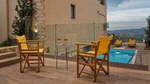 A poolside area with two yellow chairs, a glass table with two wine glasses, and a view of a swimming pool and distant landscape. - Villa Armonia Boutique Living (Chania)