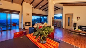 A spacious living area with a large window overlooking a scenic view, a fireplace, and a dining area with a table set for two. - Villa Armonia Boutique Living (Chania)