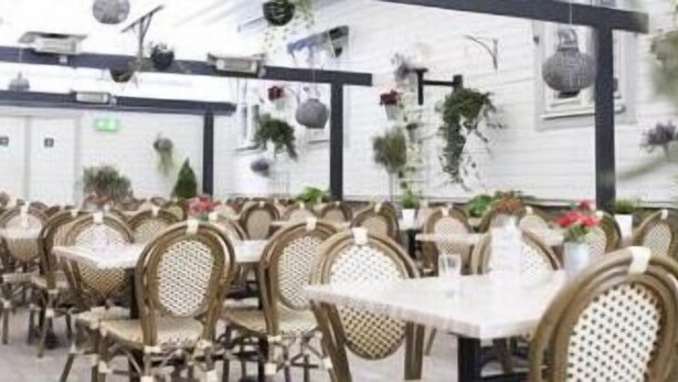 A restaurant with wicker chairs and tables, indoor plants, and a white exterior wall. - Go To Sleep Arvika - Hostel (Arvika)