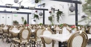 A restaurant with wicker chairs and tables, indoor plants, and a white exterior wall. - Go To Sleep Arvika - Hostel (Arvika)