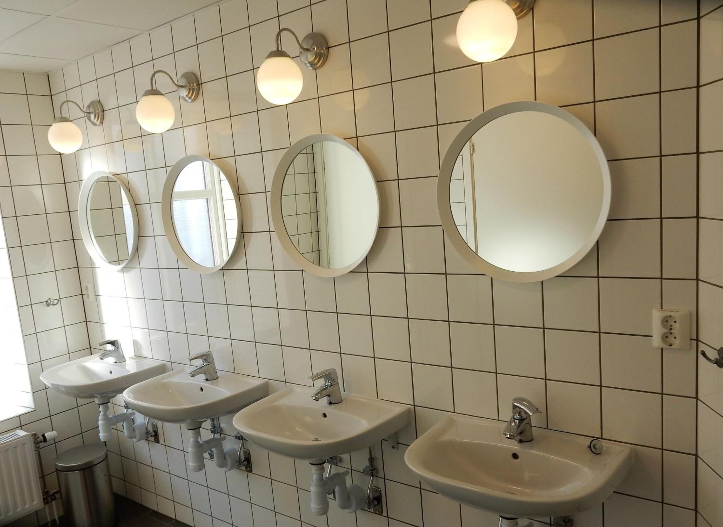 A restroom with four sinks, three round mirrors, and wall-mounted light fixtures.