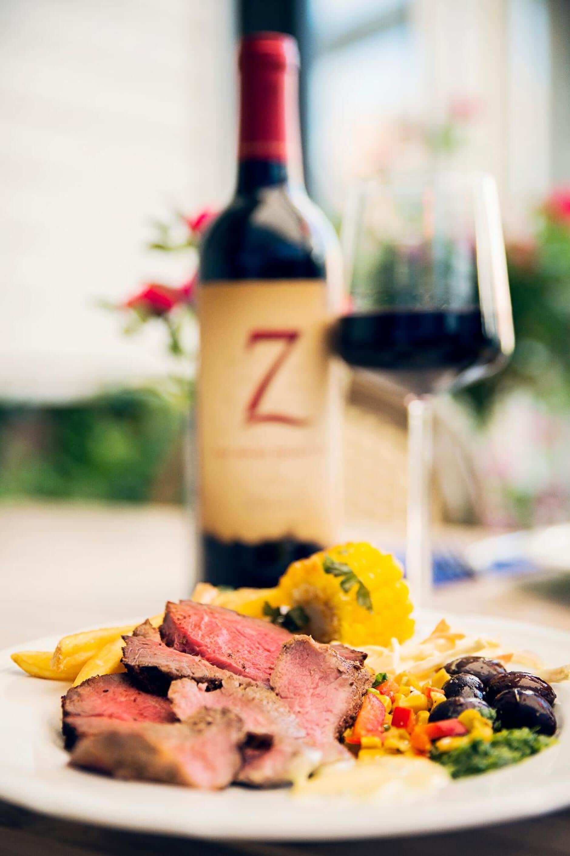 A plate of food with steak, vegetables, and a bottle of wine.