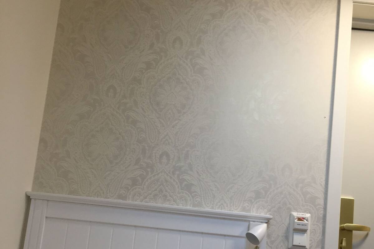 Ett hotellrum med en mönstrad tapet, en vit sänggavel och en dörr med ett guldhandtag.