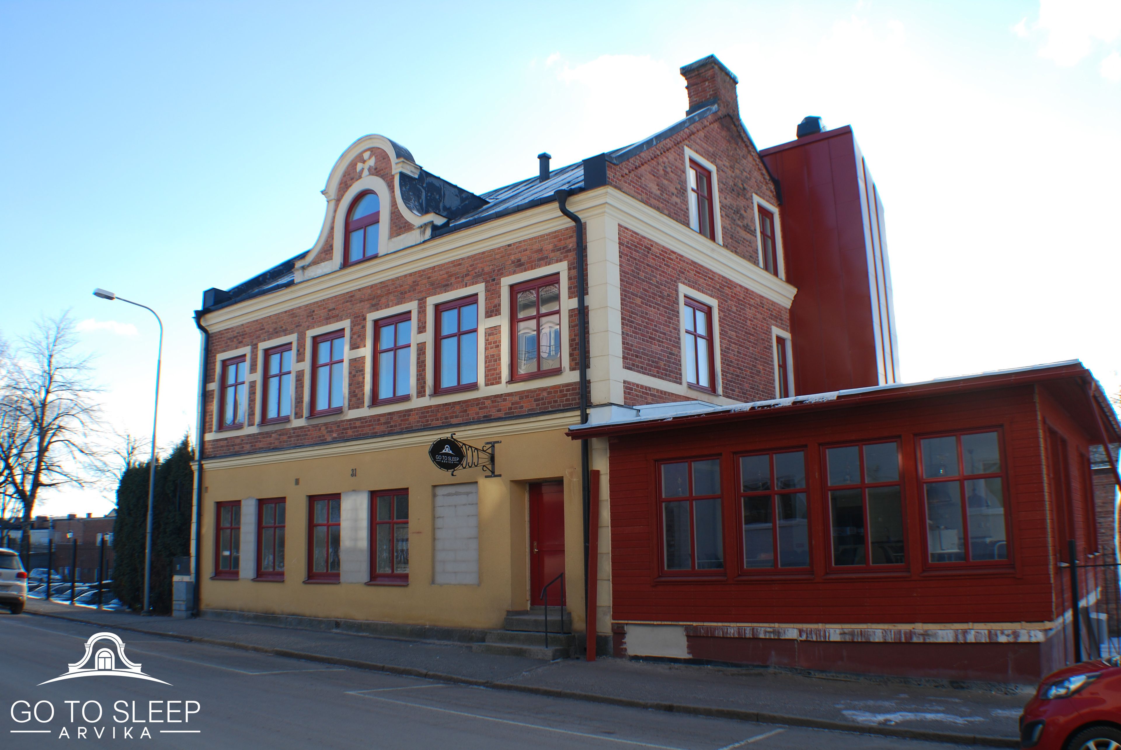 A two-story building with a yellow facade and red accents, featuring multiple windows and a visible entrance.