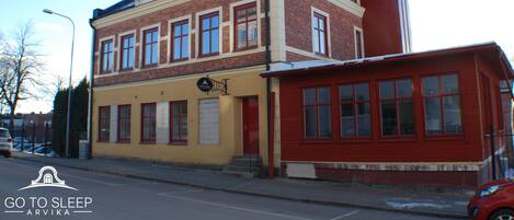 A two-story building with a yellow facade and red accents, featuring multiple windows and a visible entrance.