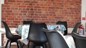 Un comedor con pared de ladrillo, sillas negras, una mesa con mantel floral y una lámpara de latón colgante.