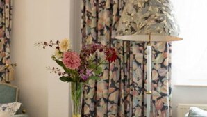 A room with floral curtains, a lamp, and a vase with flowers. - Hotel Gasthaus Schubert (Garbsen)