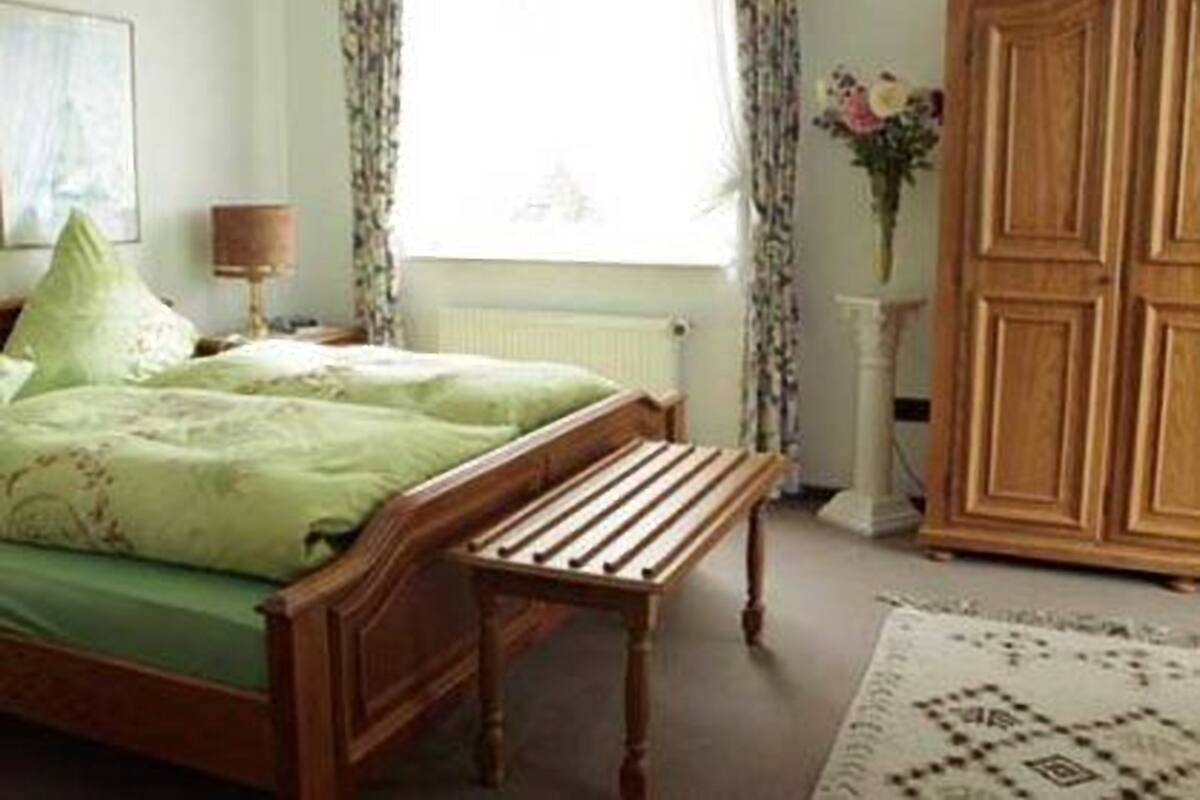 A bedroom with a wooden bed, a bench, a nightstand, a lamp, and a wardrobe.