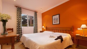 A hotel room with a large bed, a wooden nightstand, a desk, and a window with curtains. - Apt. Grande Ciruelo, A/C, community pool, Wifi, near beach 400 m (Cala Sant Vicenç)