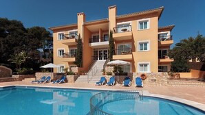 A multi-story hotel with a swimming pool, sun loungers, and a staircase leading to the entrance. - Apt. Grande Ciruelo, A/C, community pool, Wifi, near beach 400 m (Cala Sant Vicenç)