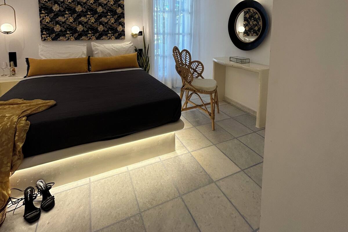 A modern bedroom with a bed, bedside table, chair, and a desk with a mirror.