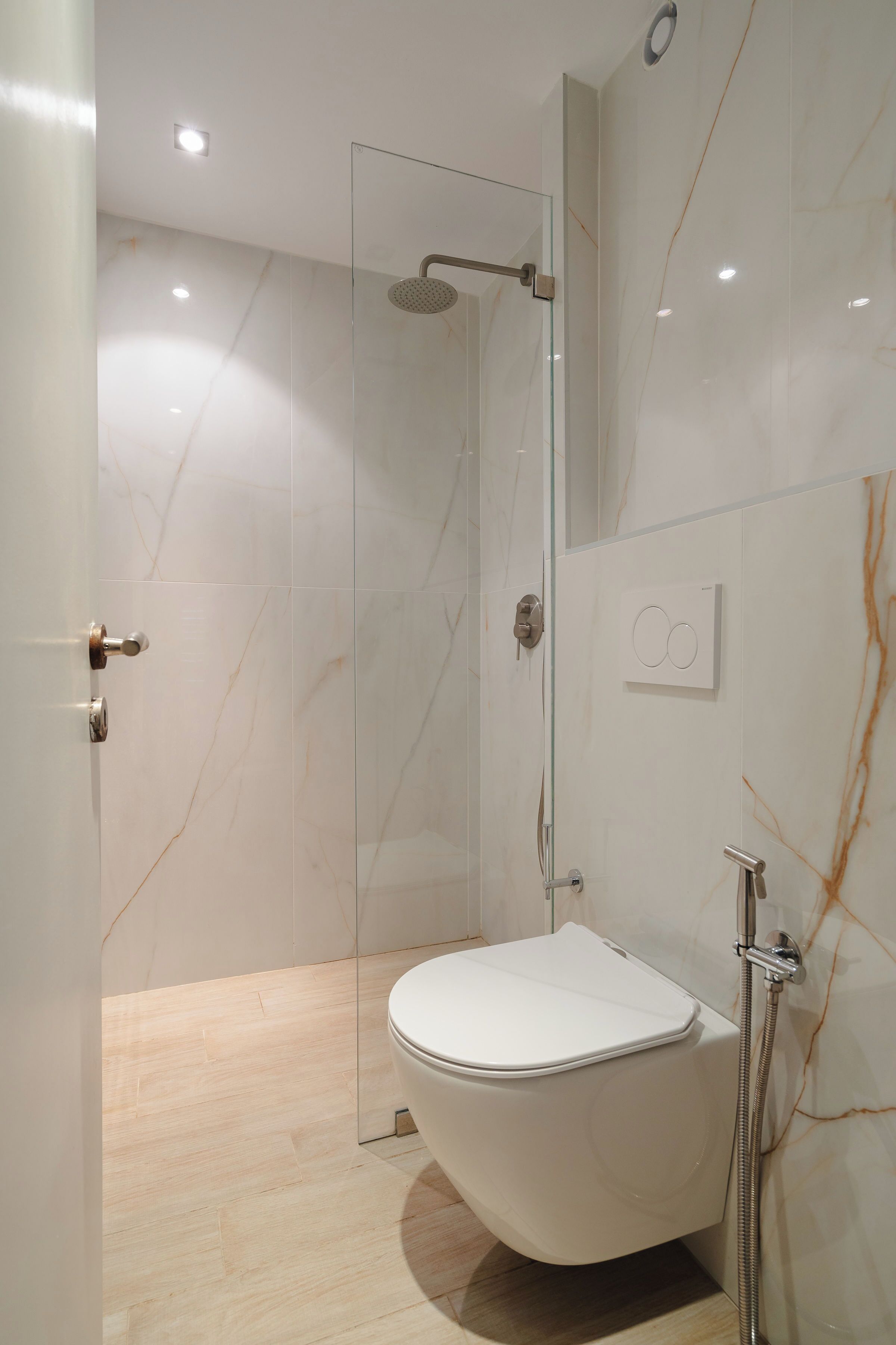 Une salle de bain moderne avec une douche à parois de verre, des toilettes et des murs en marbre.