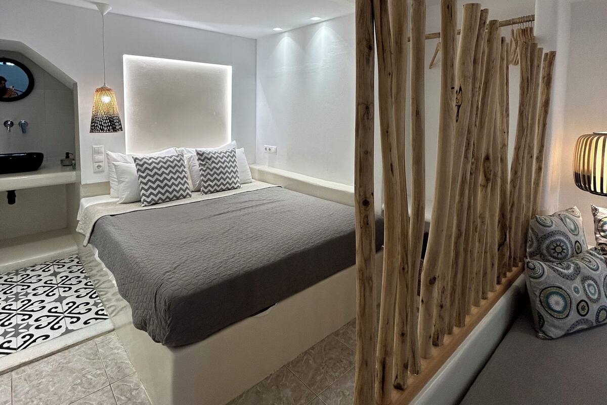 A modern bedroom with a large bed, a bedside table, a mirror, and a wooden partition.